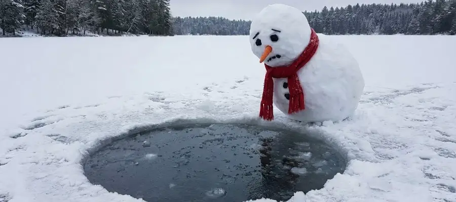 En snögubbe står vid en isvak och tittar ner. Han ser lika förväntansfull ut som jag skulle ha gjort inför ett bad.