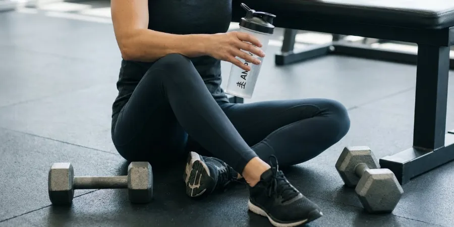 Vilopaus på gymmet. En kvinna har slagit sig ner med sin shaker efter några tunga lyft och tar igen sig innan det är dags för nästa satsning.
